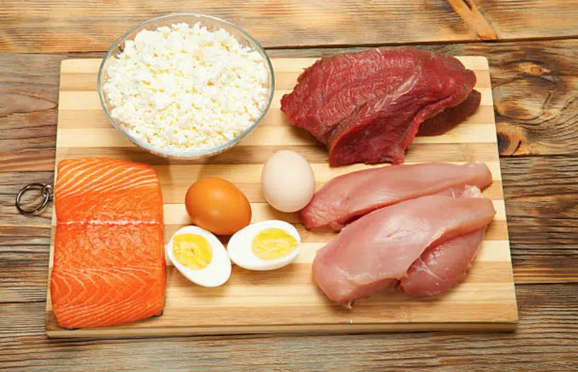 Une table avec de nombreux aliments riches en protéines : de la viande rouge, du poulet, du saumon et des œufs.