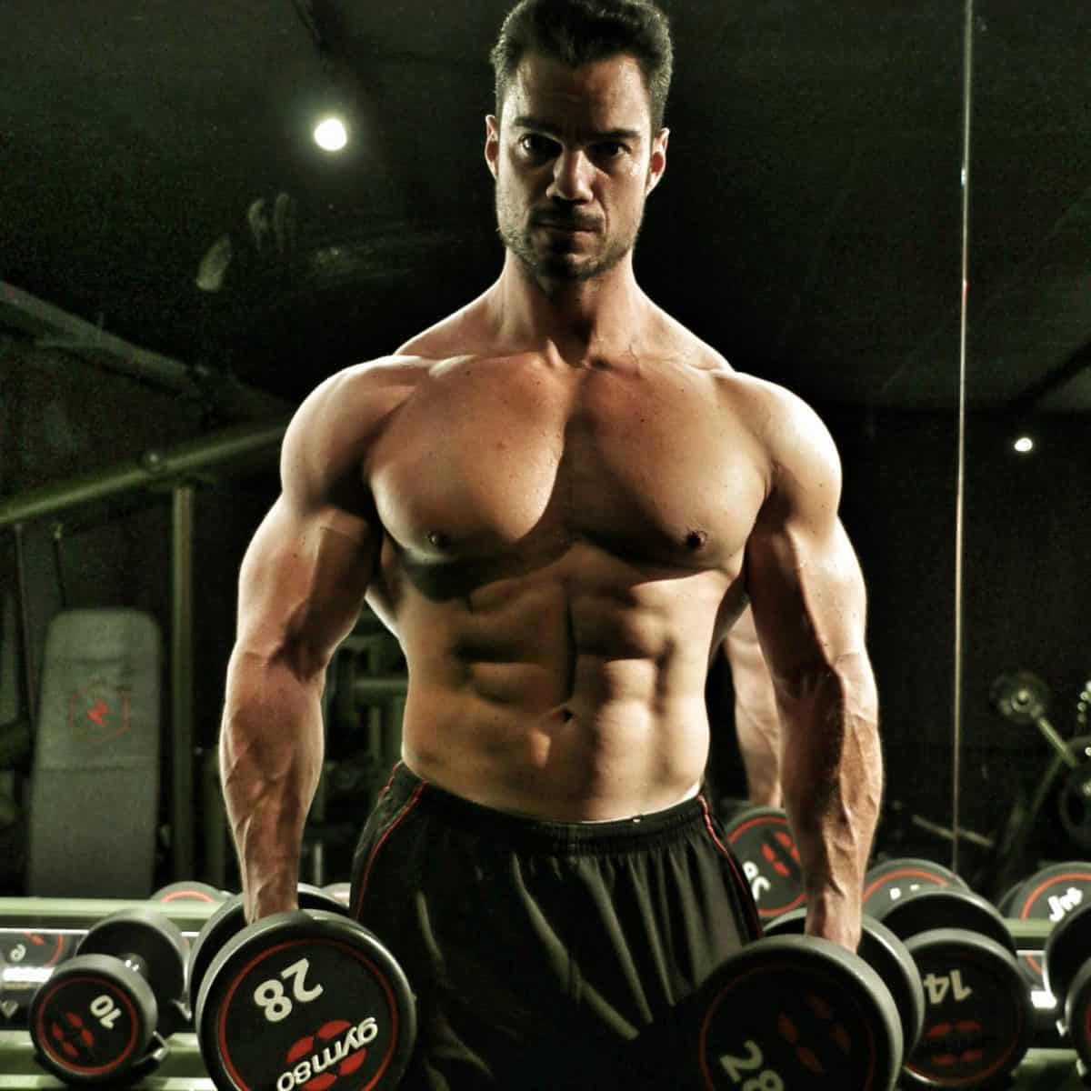 Julien Quaglierini shirtless with dumbbells in his hands.