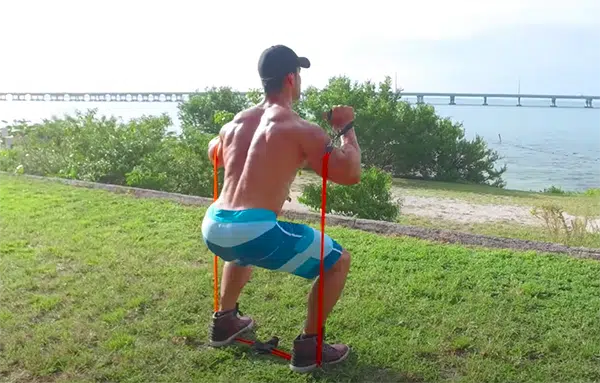 Un homme effectue des squats avec une bande élastique devant l'océan.