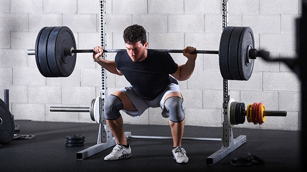 An athlete performs the squat exercise with a weight bar in a gym.