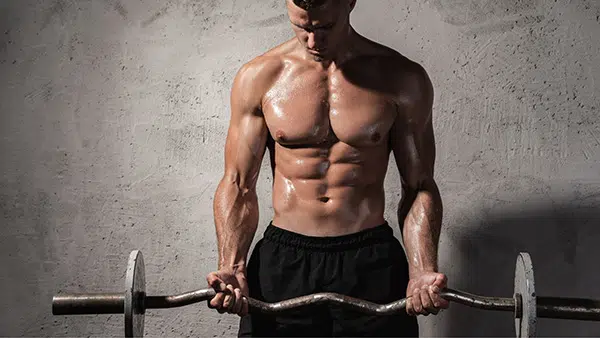 Un homme réalise l'exercice de musculation du curl biceps torse nu.
