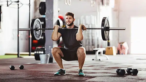 Un homme fait l'exercie de musculation du squat dans une salle de sport.