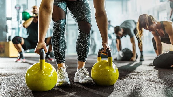 Un sportif s'apprête à soulever 2 kettlebells de couleur jaune dans une salle de fitness.