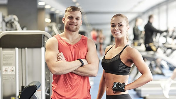 2 coachs sportifs (1 homme et une femme) dans une salle de fitness et de musculation.