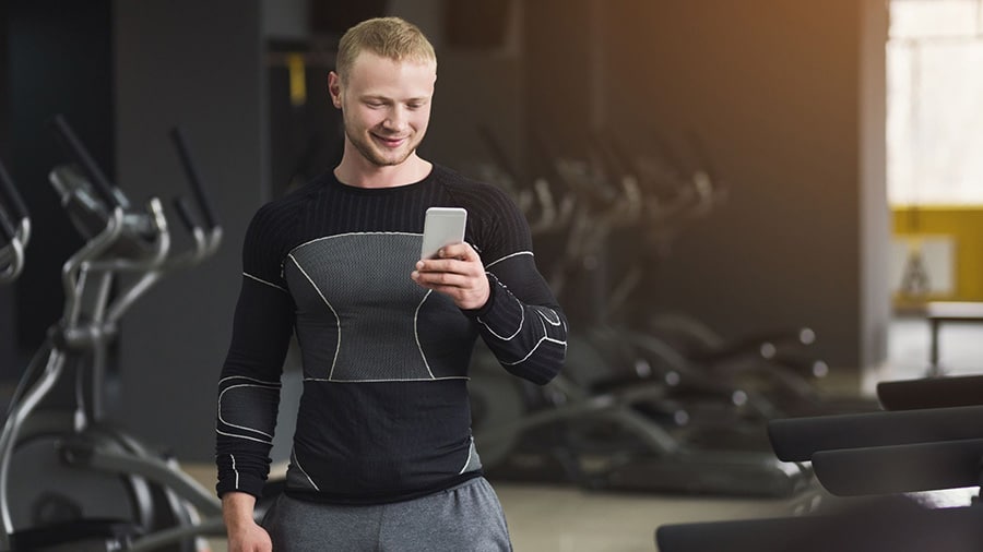 Un homme dans une salle de sport consulte sur son smartphone la meilleure application de musculation.