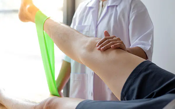 Un kinésithérapeute effectue un exercice pour les jambes avec un patient blessé à l'aide d'un élastique de fitness.