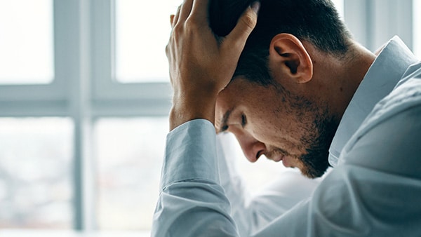A stressed man holds his head in his hands.