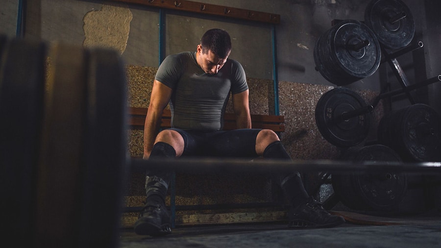 An athlete sitting on a bench in a weight room, in full mental preparation for the sport.