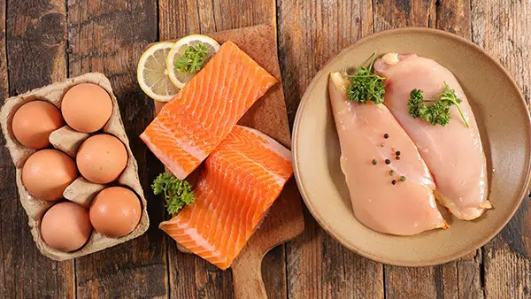 Des aliments riches en protéines disposés sur une table : oeufs, saumon et blancs de poulet.