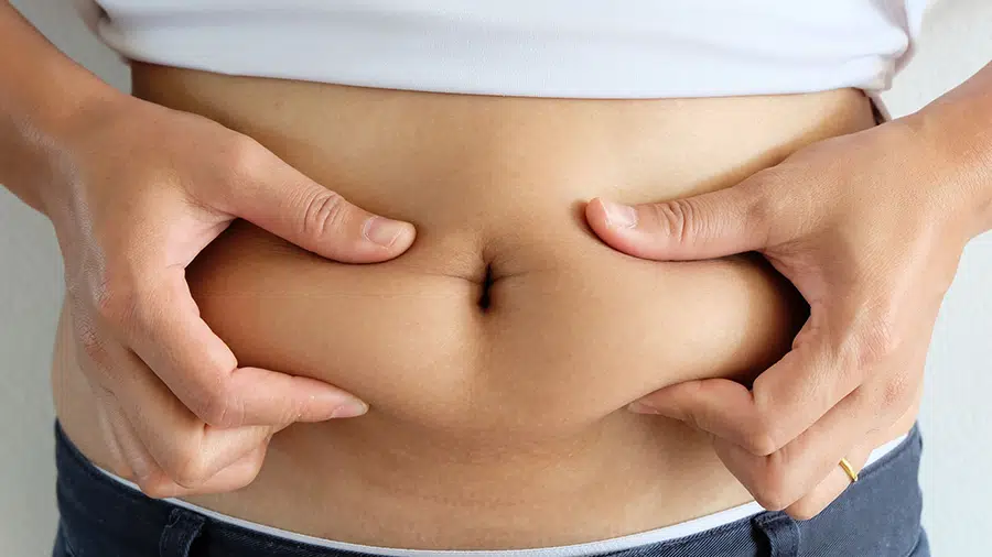 Une personne se tient la graisse abdominale entre les deux mains et se demande comment perdre le gras du ventre.