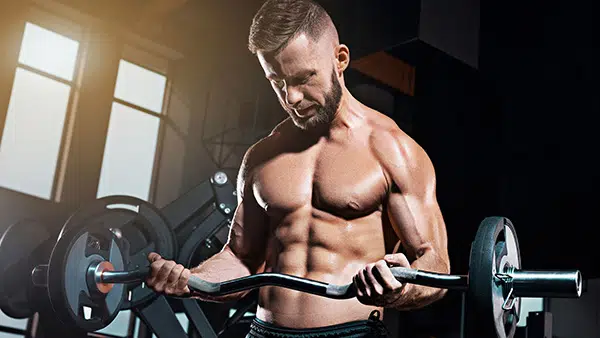 Un homme torse nu, muscles et abdominaux saillants, fait un exercice de musculation pour les biceps.