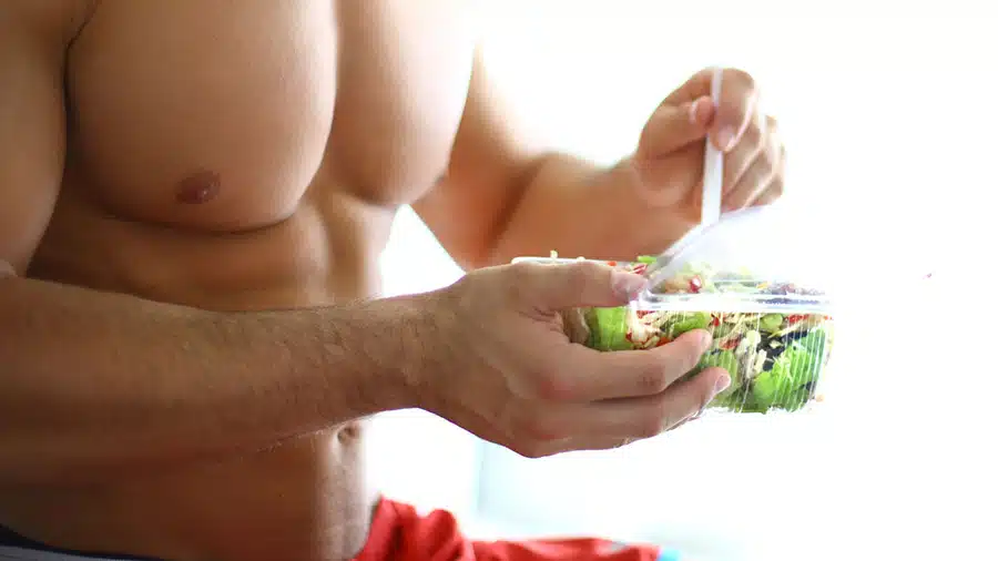 Un homme musclé torse nu mange un repas pour remplir ses stocks de glycogène.