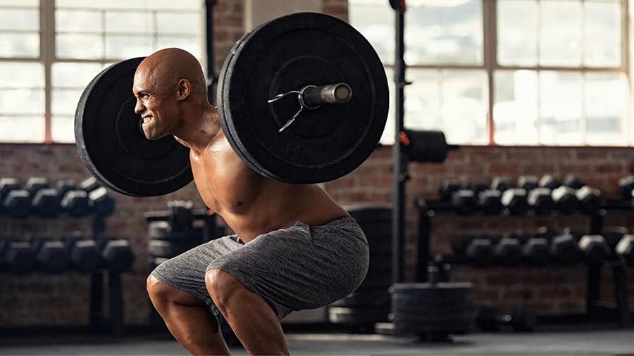 Un homme torse nu utilise la technique du rest pause sur l'exercice de musculation du squat dans une salle de sport.