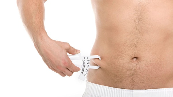 Un homme torse nu mesure son taux de masse grasse au niveau du ventre avec une pince à pli cutané.