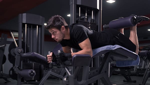 Un homme réalise l'exercice du leg curl allongé dans une salle de musculation pour renforcer ses ischios.