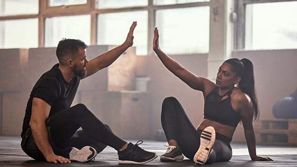 Dans une salle de fitness, deux sportifs (un homme et une femme) sont assis sur le sol et se tapent dans la main.
