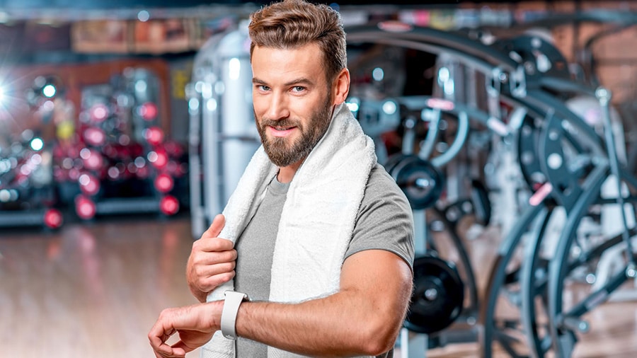 Un homme dans une salle de musculation, serviette de sport autour du cou, prêt à s'entraîner et à tenir ses résolutions sportives.
