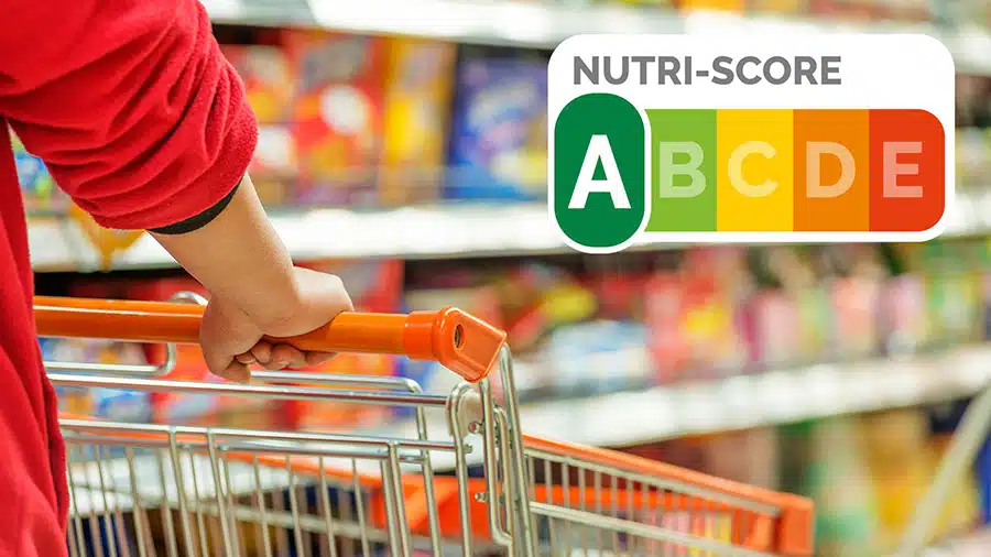 Une personne pousse un chariot dans le rayon d'un supermarché, avec le logo du Nutri-score placé en haut à droite de l'image.
