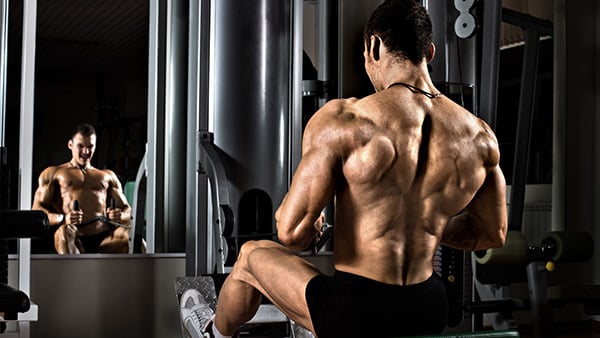 Un homme torse nu dans une salle de musculation effectue un mouvement de tirage horizontal pour le dos en superset.