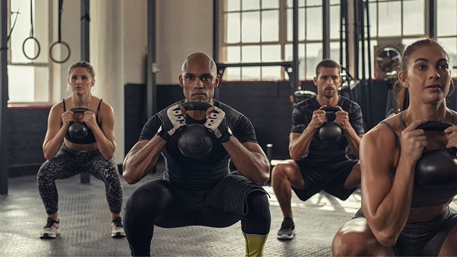 A group of 4 athletes (2 men and 2 women) perform the kettlebell squat as part of AMRAP training.