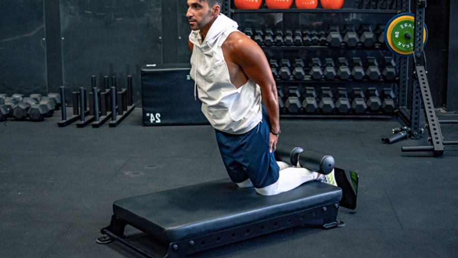 A man in a gym performs the nordic curl exercise to strengthen his hamstrings.