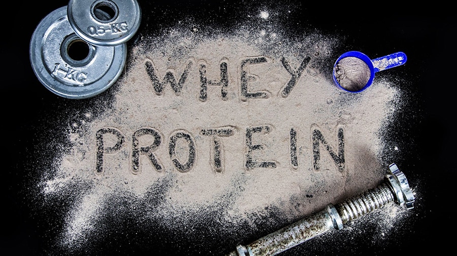 En haut à gauche, des disques de poids. En haut à droite, un doseur pour les compléments alimentaires. Au centre, de la protéine en poudre dans laquelle il est écrit "whey protein".