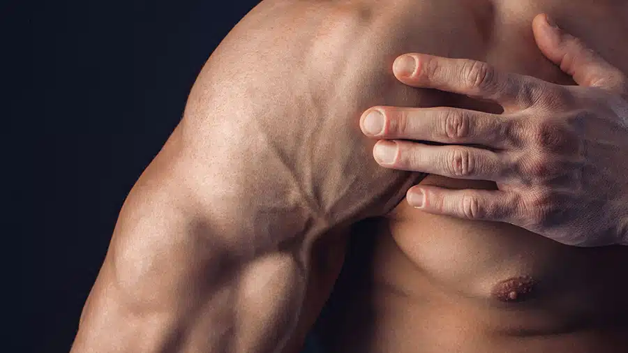 Un home torse nu, victime de courbatures, se tient le muscle pectoral droit avec sa main gauche.