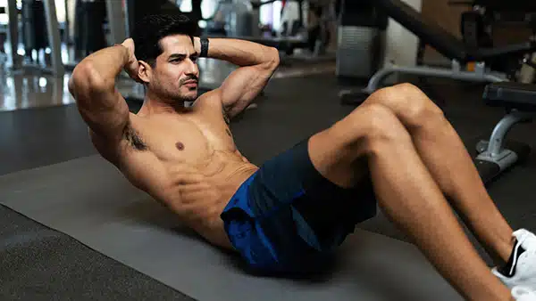 Un homme torse nu effectue l'exercice des crunchs pour muscler ses abdominaux dans une salle de fitness et de musculation.