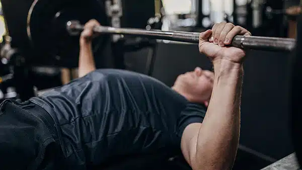 Un athlète dans une salle de sport réalise l'exercice de musculation du développement couché à la barre pour les pectoraux.