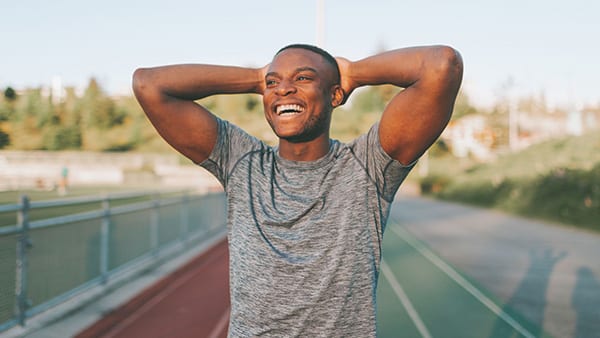 Un sportif sur une piste d'athlétisme souriant après avoir effectué une séance de sport grâce à la sécrétion de dopamine naturelle.