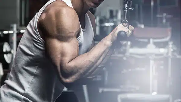 Un sportif en débardeur effectue l'exercice de musculation des extensions triceps à la poulie haute.
