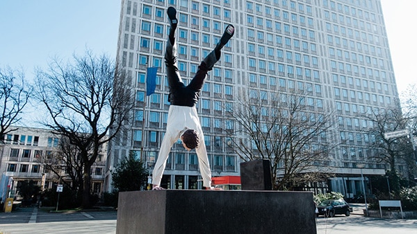A man makes the handstand figure on a concrete block in front of a building.