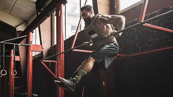 Un homme portant un gilet lesté effectue un muscle up dans une salle de fitness et de musculation.