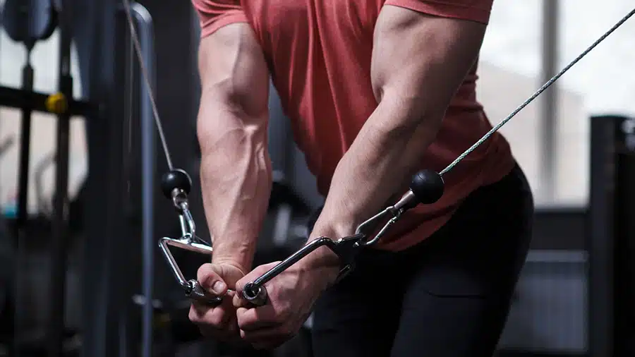 Un pratiquant de musculation portant un t-shirt rouge exécute un exercice de musculation pour les pectoraux à la poulie vis-à-vis.