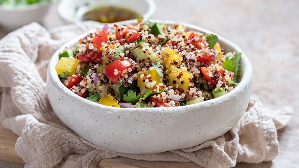 A bowl with salad with quinoa, tomatos, mango and some aromatic herbs.