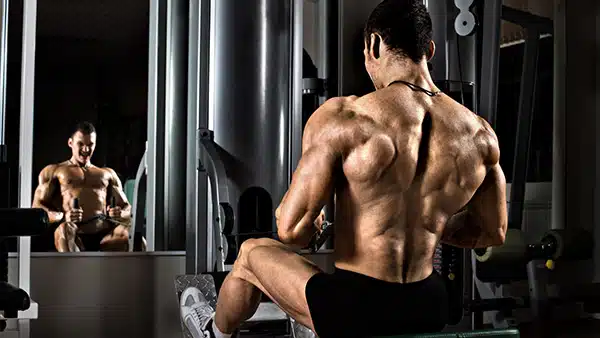 Un homme torse nu réalise un exercice de tirage horizontal à la poulie de musculation dans une salle de fitness.