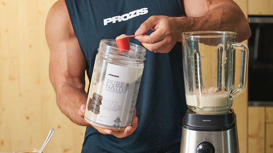 Sports coach Julien Quaglierini, wearing a Prozis tank top, adds a dose of whey protein to a blender.