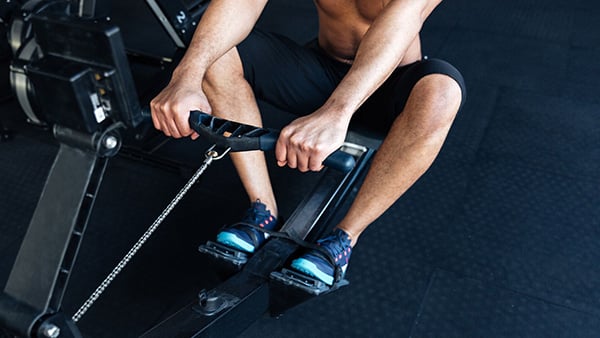 A shirtless man does a cardio warm-up on a rowing machine in a fitness center.