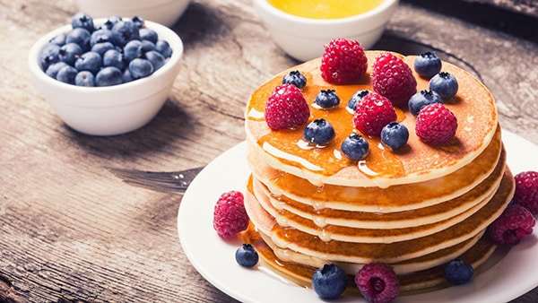 A plate full of healthy pancakes, sprinkled with blueberries and raspberries.