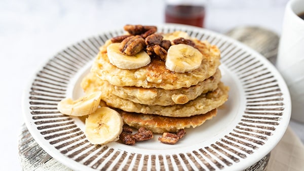 A plate with 4 protein pancakes, topped with banana and oilseeds.