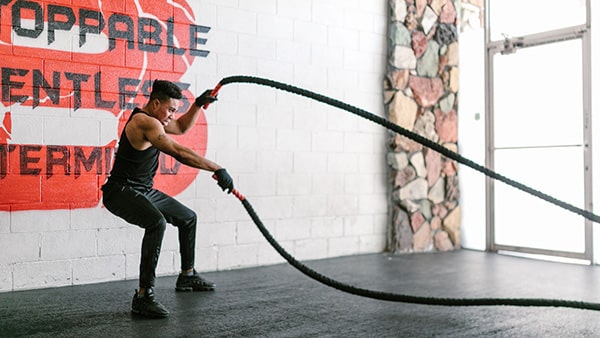 A man in a fitness center exercises with a battle rope.