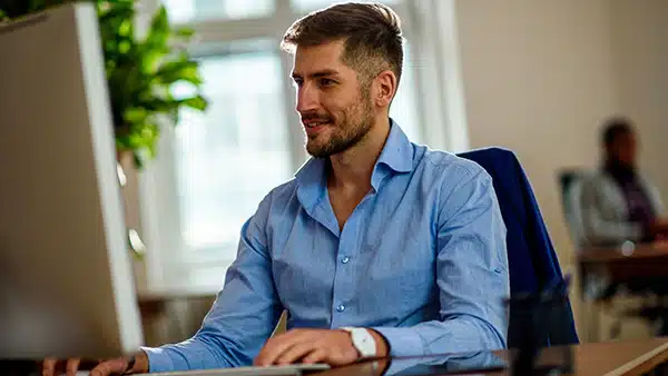 Un homme vêtu d'une chemise bleue, en train de travailler assis devant un ordinateur, ce qui peut causer une baisse de testostérone.
