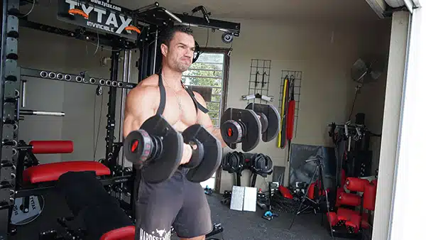 Le coach sportif Julien Quaglierini effectuant un exercice de curl biceps avec des haltères et un arm blaster.