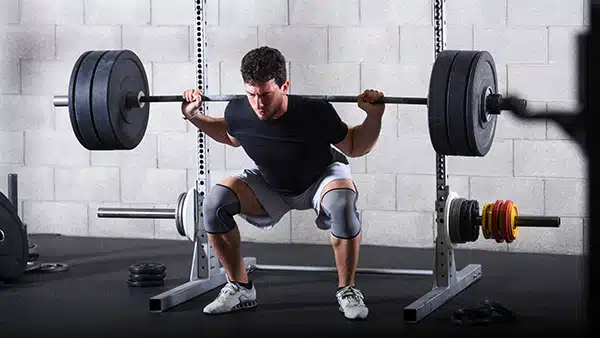 Un homme fait du squat dans une salle de fitness.