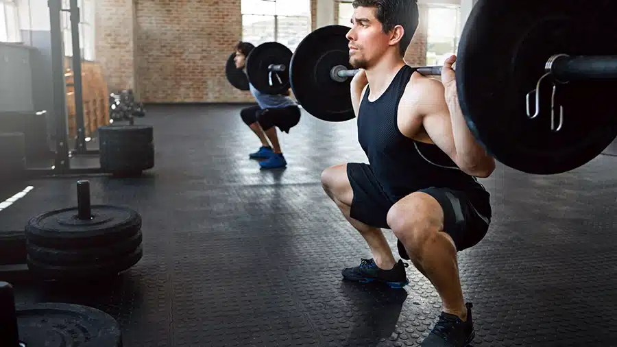 Dans une salle de musculation, deux hommes effectuent des squats profonds grâce à une bonne mobilité de cheville.