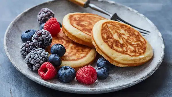 Une assiette avec 3 pancakes, accompagnés de fruits rouges.