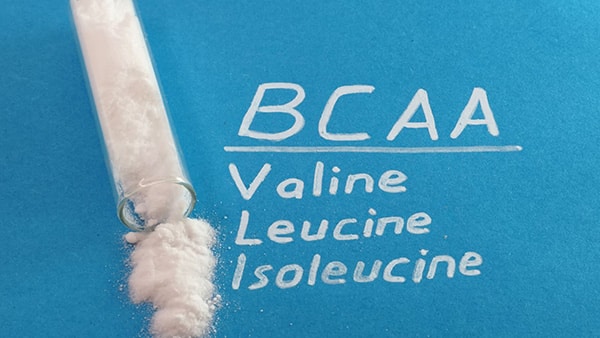 A tube of powder on a blue background, with the names of the 3 BCAAs next to it: valine, leucine and isoleucine.