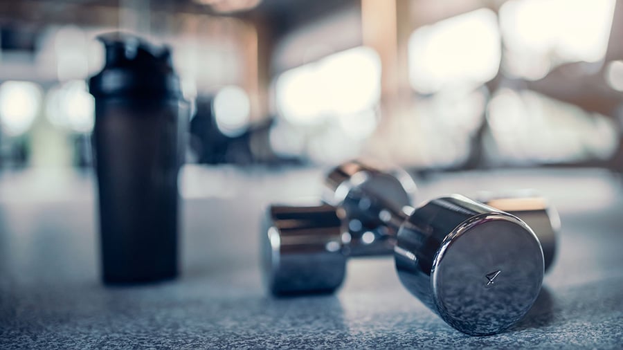Dumbbells and a water bottle on the floor of a weight room: two sporty gift ideas for a loved one.