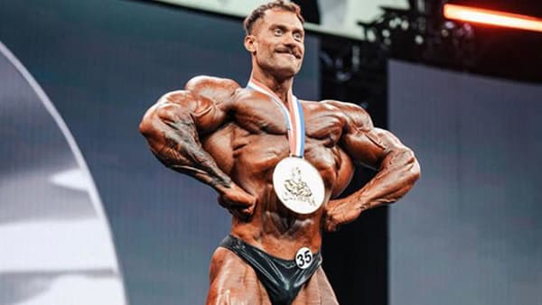 Le bodybuilder canadien Chris Bumstead, torse nu sur scène et médaille autour du cou après sa victoire au Mr Olympia 2023.