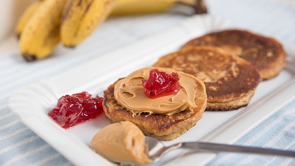 3 pancakes on a plate, 1 covered with peanut butter, with bananas at the bottom.